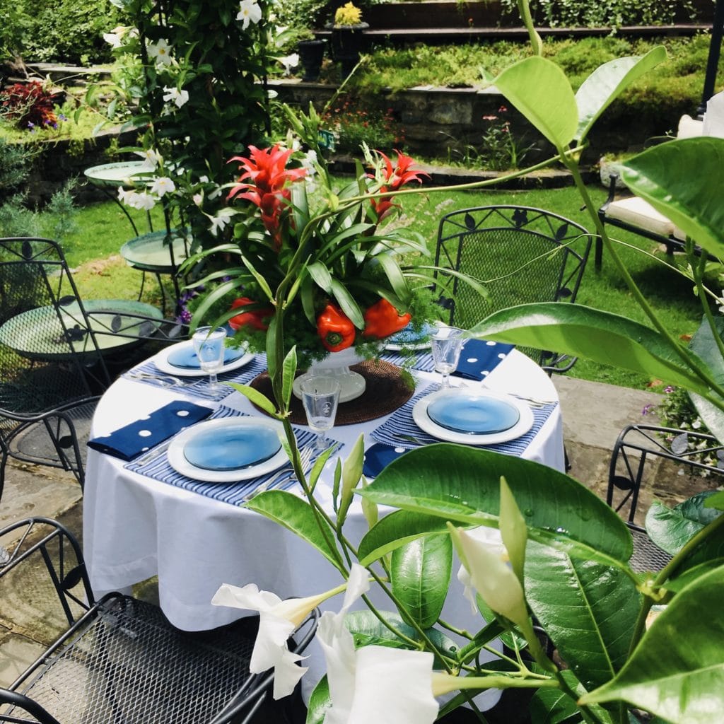 memorial day outdoor garden table setting with white tablecloth, blue napkins and placemats, and red bromeliad and red pepper centerpiece