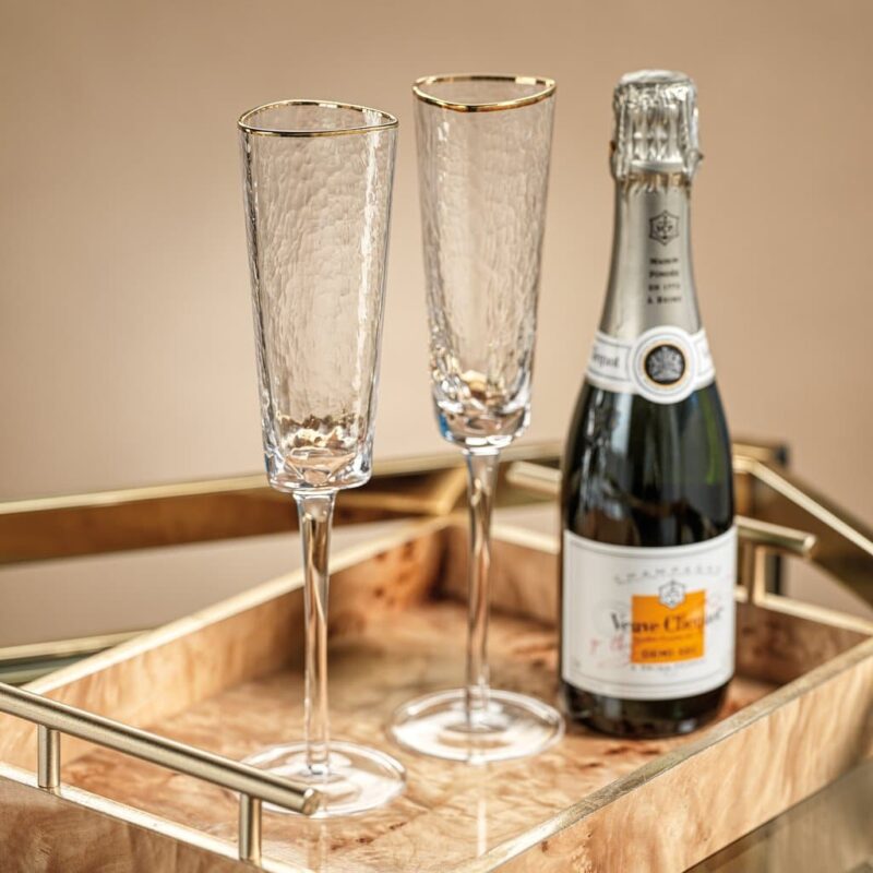 two clear triangular stemmed champagne flutes with gold rim displayed with a bottle of Veuve Cliquot