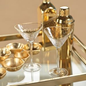 two gold-rimmed, triangular-shaped, stemmed martini glasses displayed on a gold bar cart