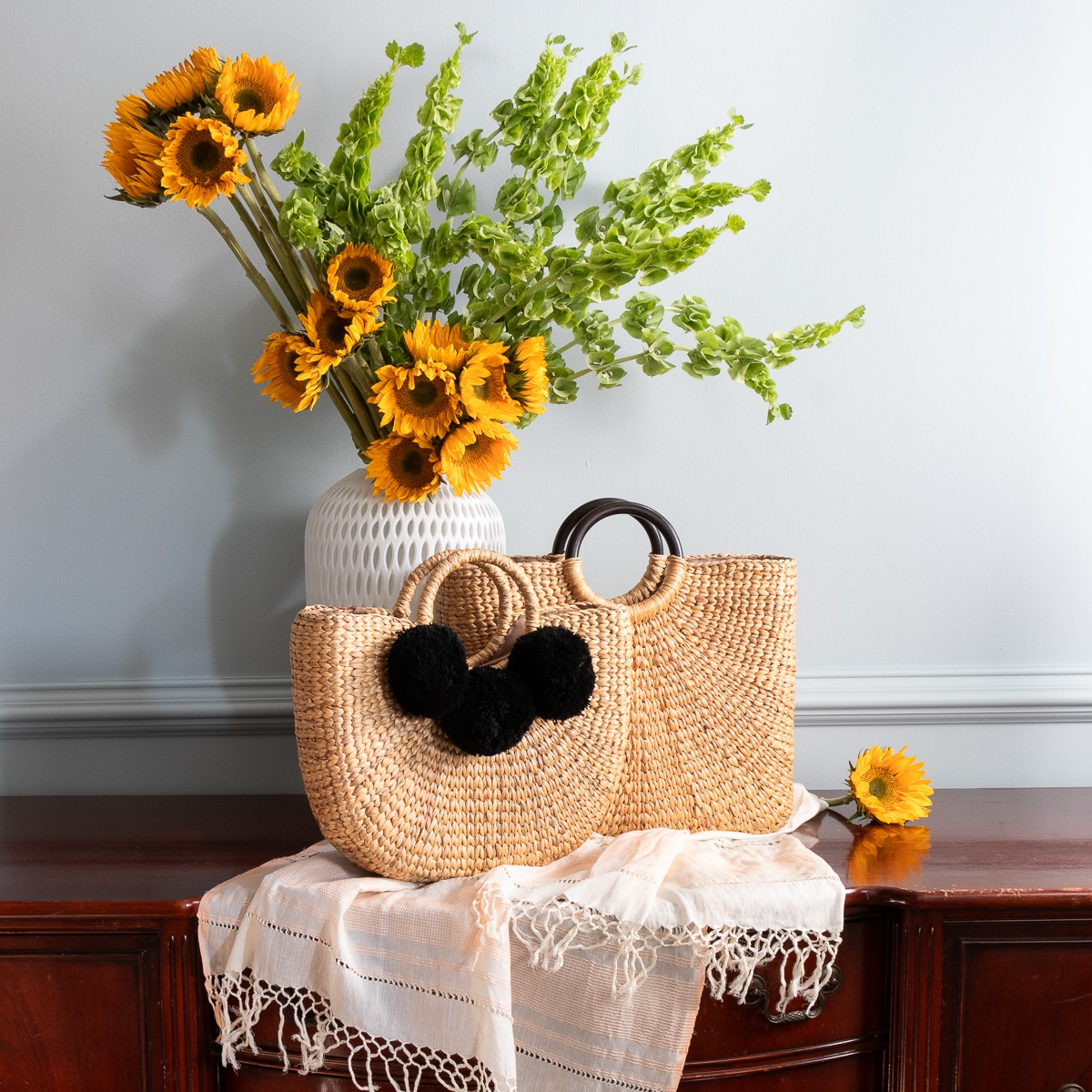 Hand Bags Image of two handbags each i our collection. The bags are straw grass. One features stained wooded handels in a ring design. The other straw handles with black poly cotton pom-poms on the front. very fun and summer stylish