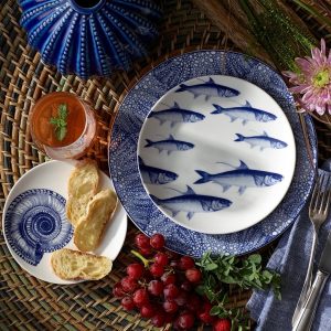 Coastal dishes of fish and shells in blue ink design displayed with fruit and drink